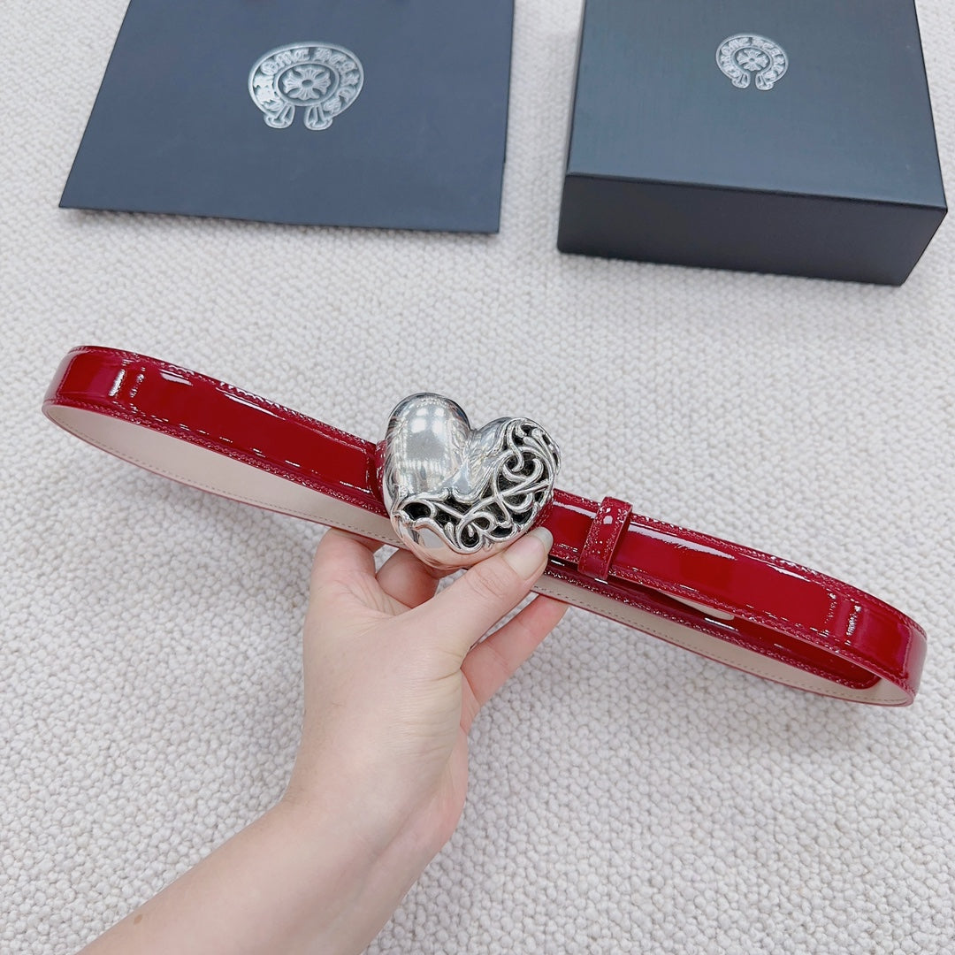 Red patent leather belt with silver heart buckle in close-up, held in hand.