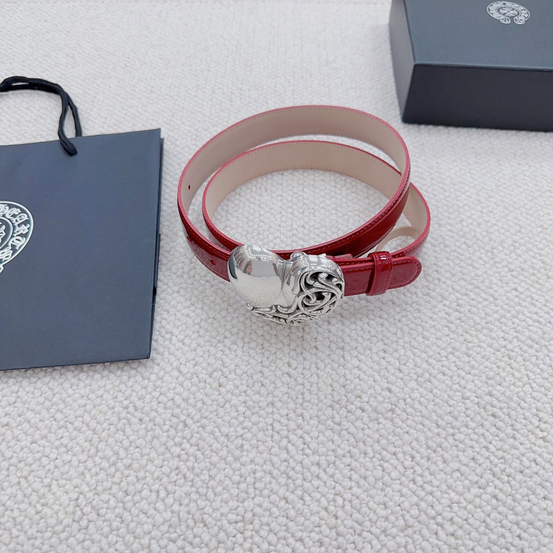 Red patent leather belt cuff with silver heart buckle, resting on fabric.