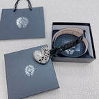 Chrome belt with glossy black strap and silver heart buckle, shown laid in a box.