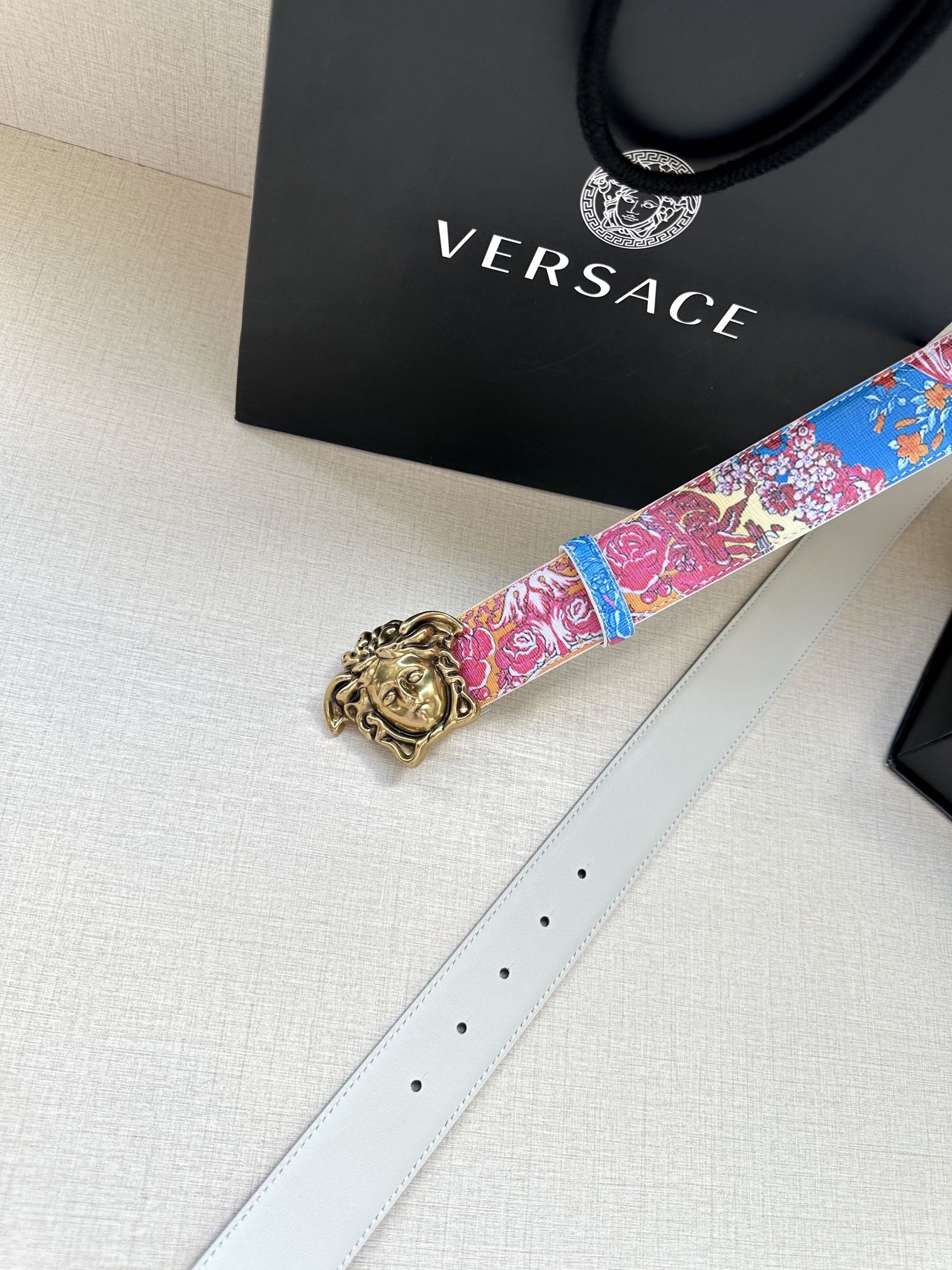 Blue and pink patterned belt with gold buckle and white leather strap, side view