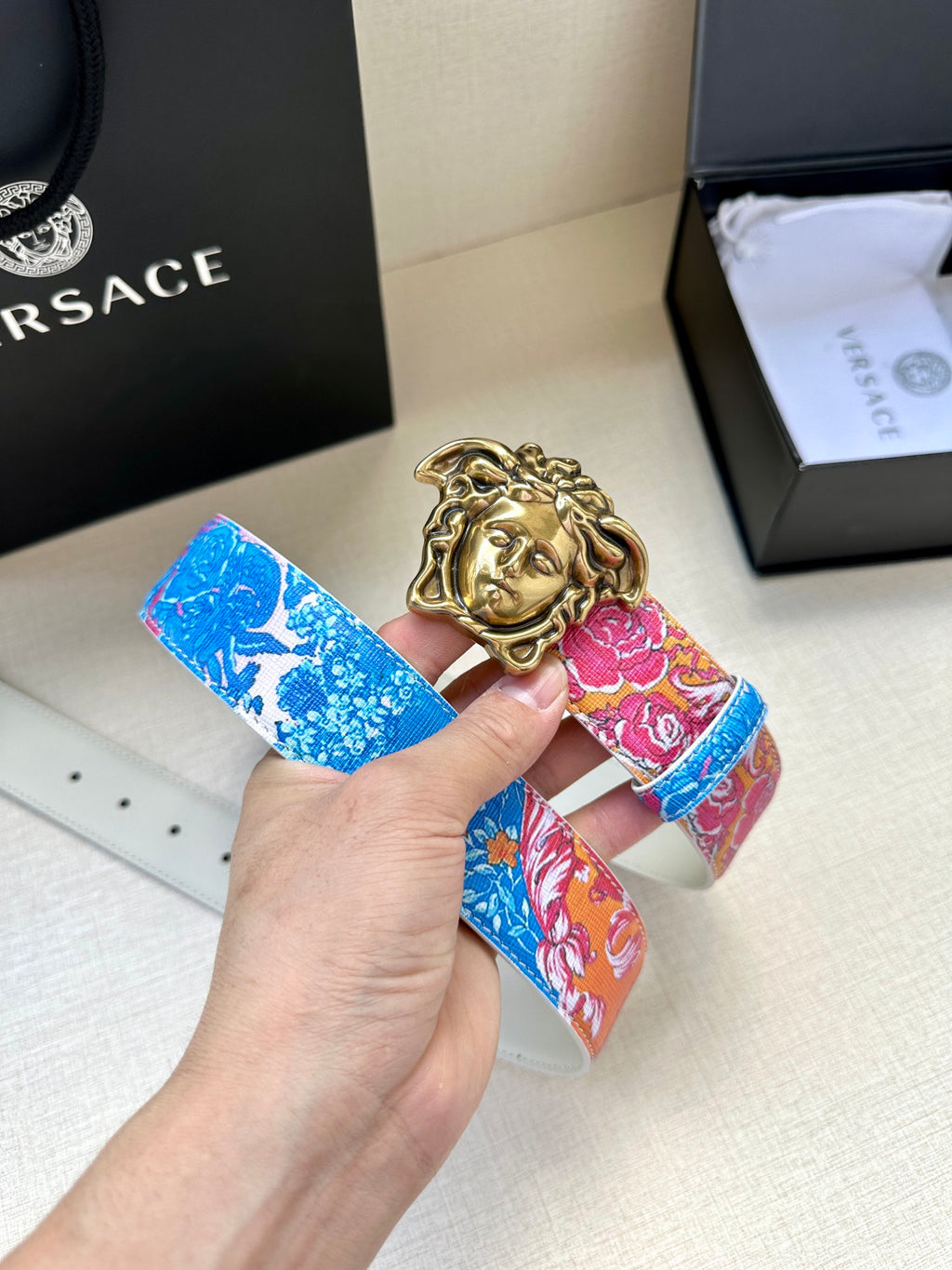Blue and pink patterned belt with gold Medusa-head buckle held in a hand