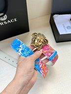 Blue and pink patterned belt with gold Medusa-head buckle held in a hand
