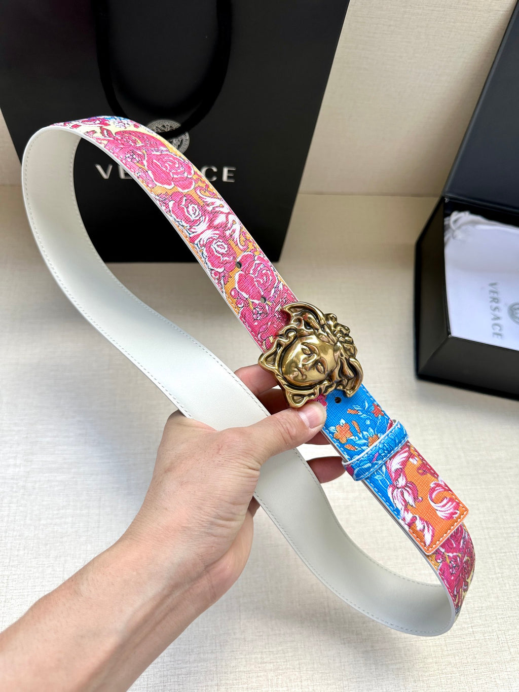 White leather belt with pink and blue patterned strap and gold lion-head buckle