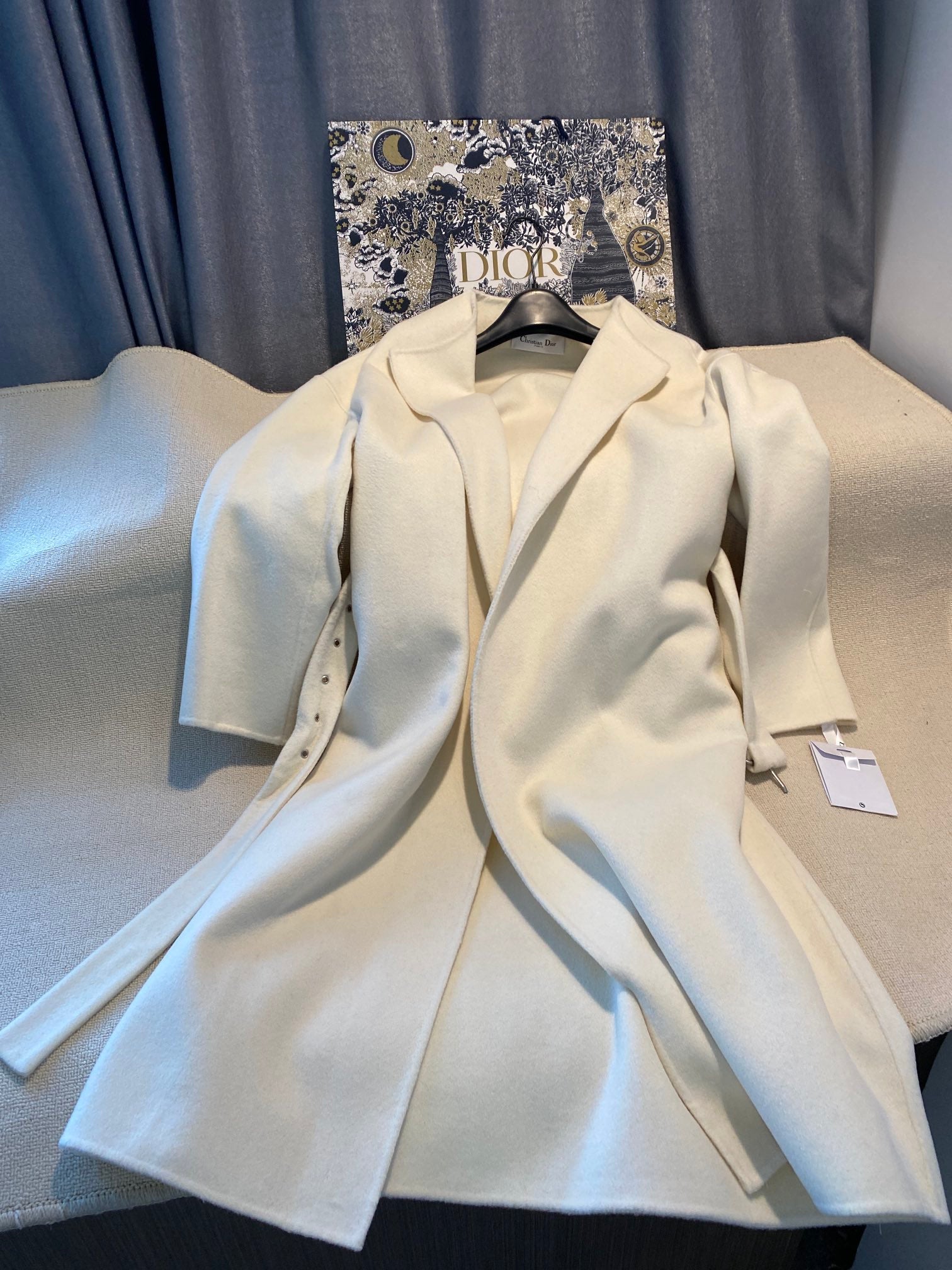 Cream long coat with notched lapels, front button closure, and matching belt