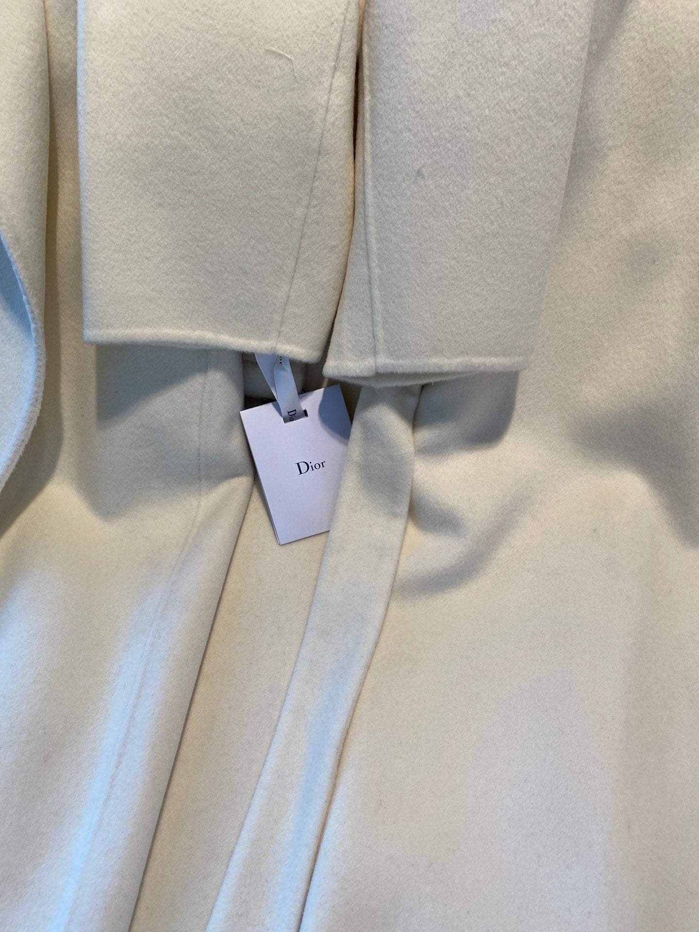 Cream long coat with hanging Dior tags at center seam