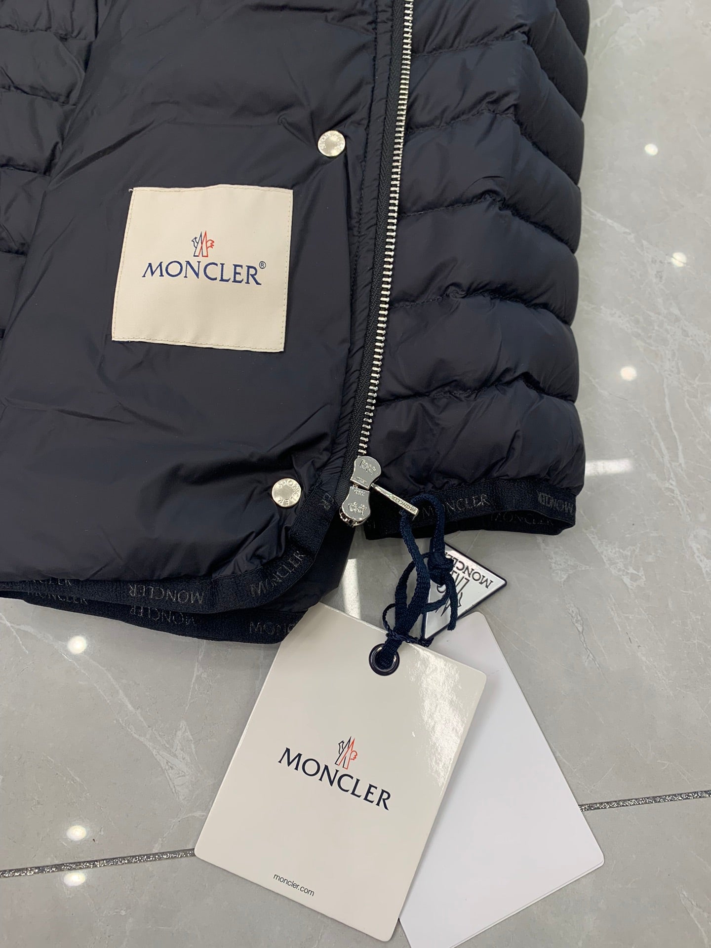 Moncler puffer jacket close-up with front zipper, drawcord hood, and tags
