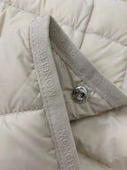 Close-up of beige quilted puffer coat shoulder with logo tape and metal button