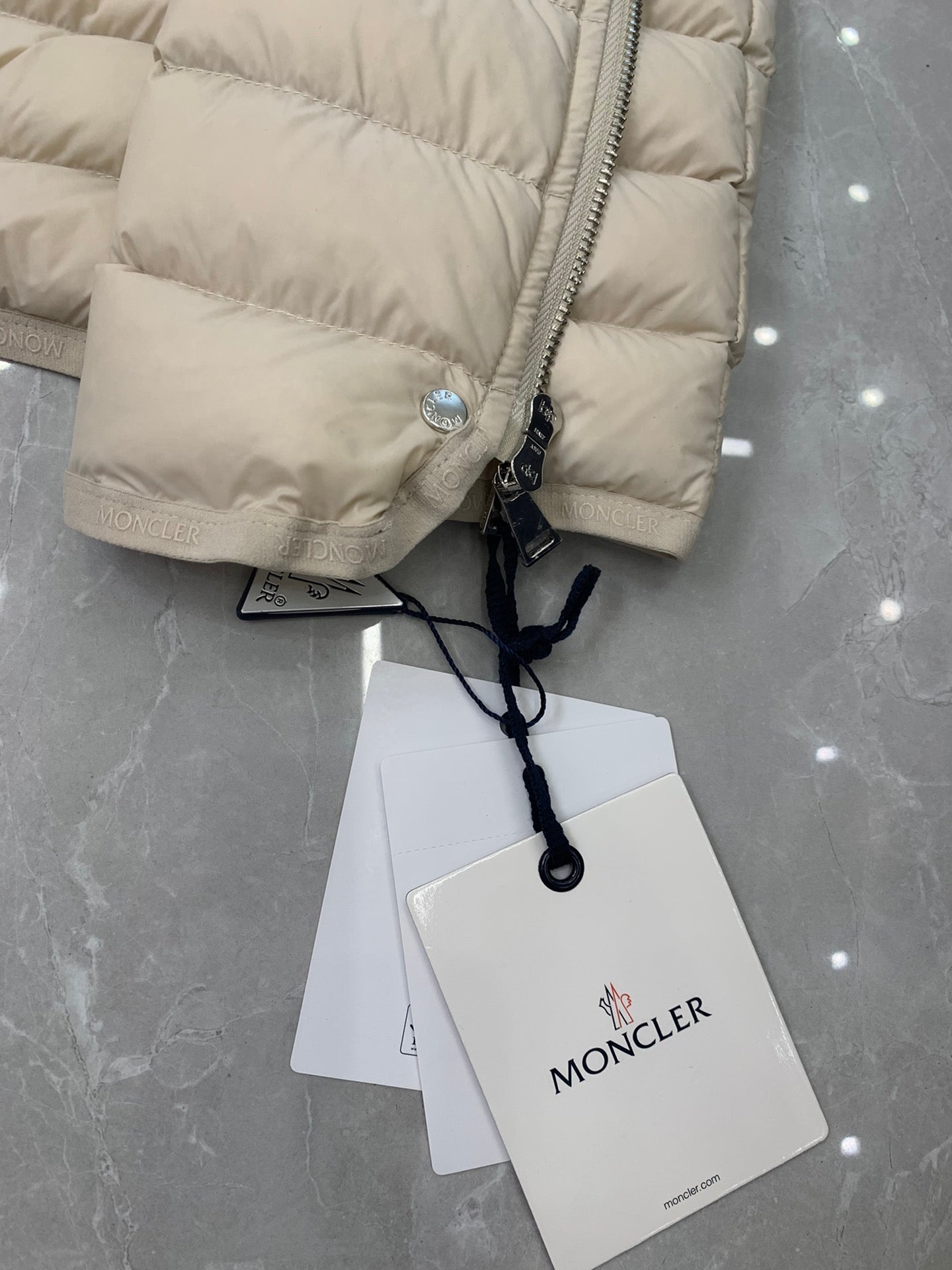 Close-up of beige quilted puffer coat sleeve cuff with Moncler patch and tags