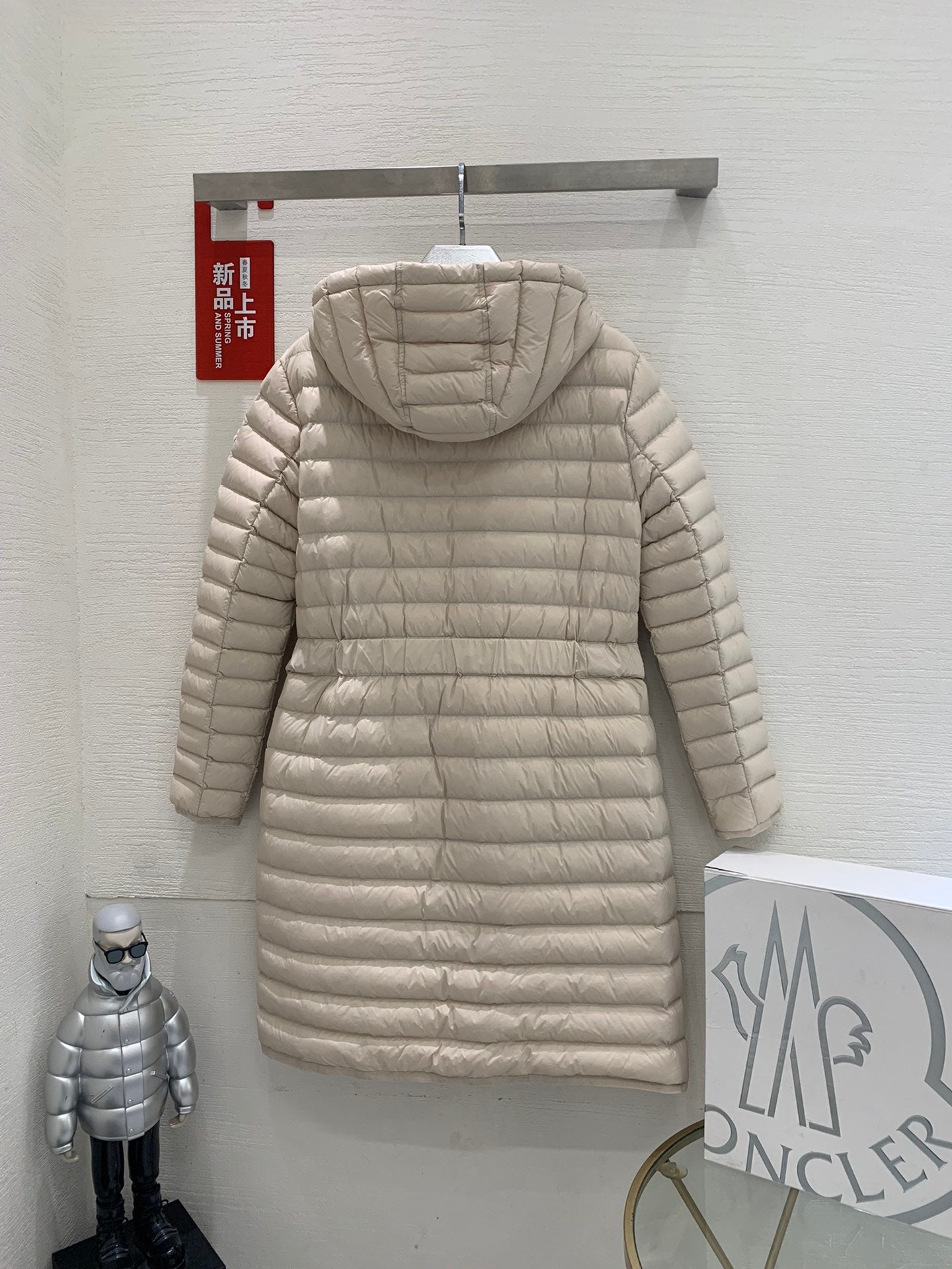 Long beige quilted puffer coat with hood, full-length zipper, and adjustable belt