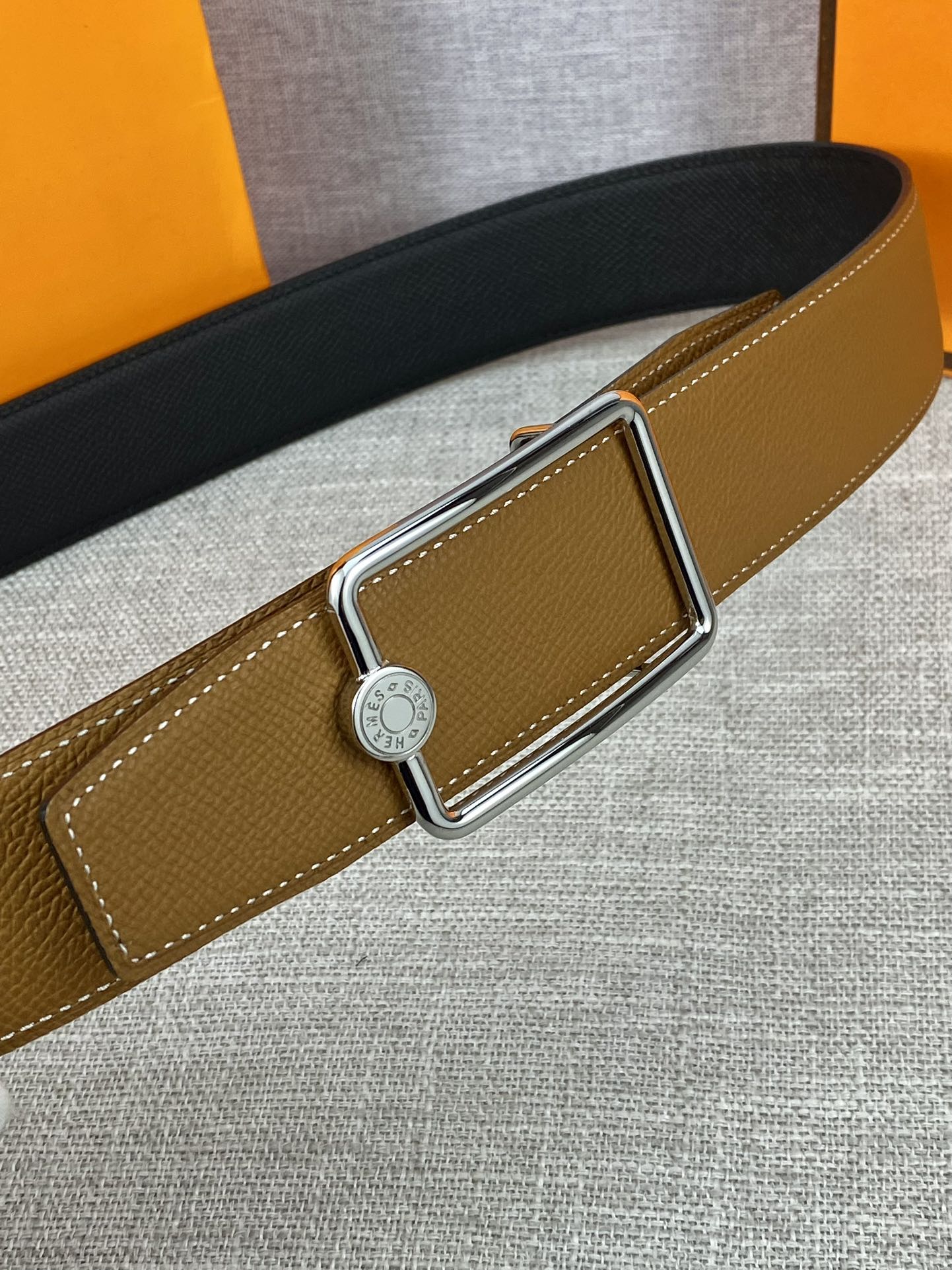 Tan leather belt with gold-tone buckle and round logo center detail