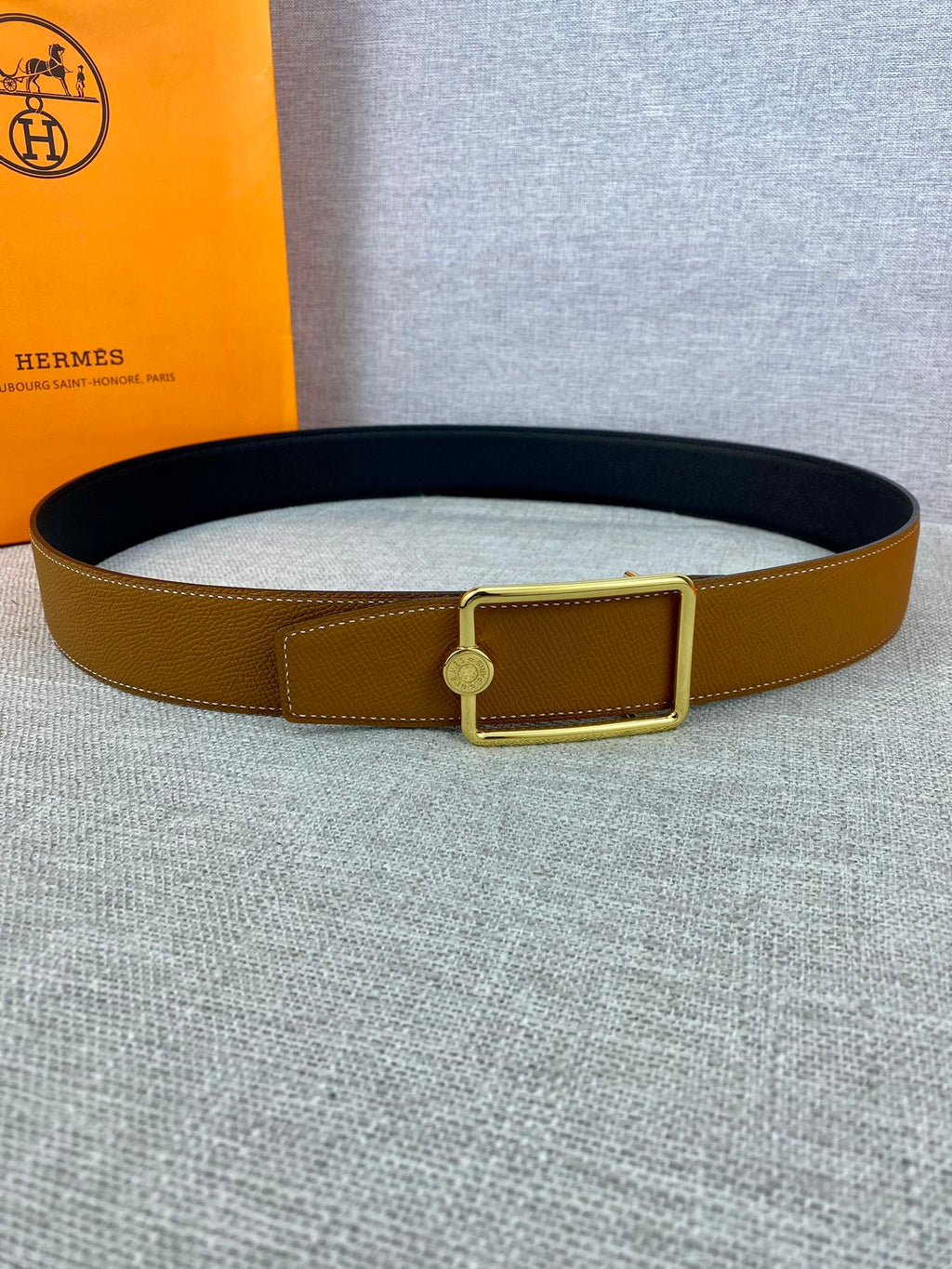 Tan leather belt with gold-tone square buckle and centered round logo cap