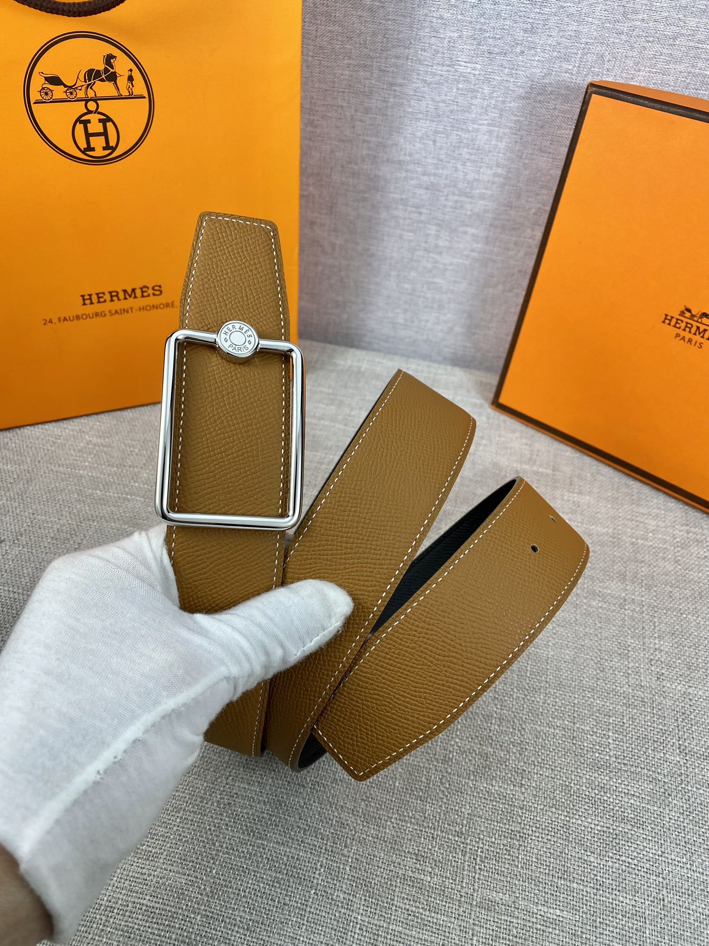 Tan leather belt with silver-tone buckle frame and round logo plate