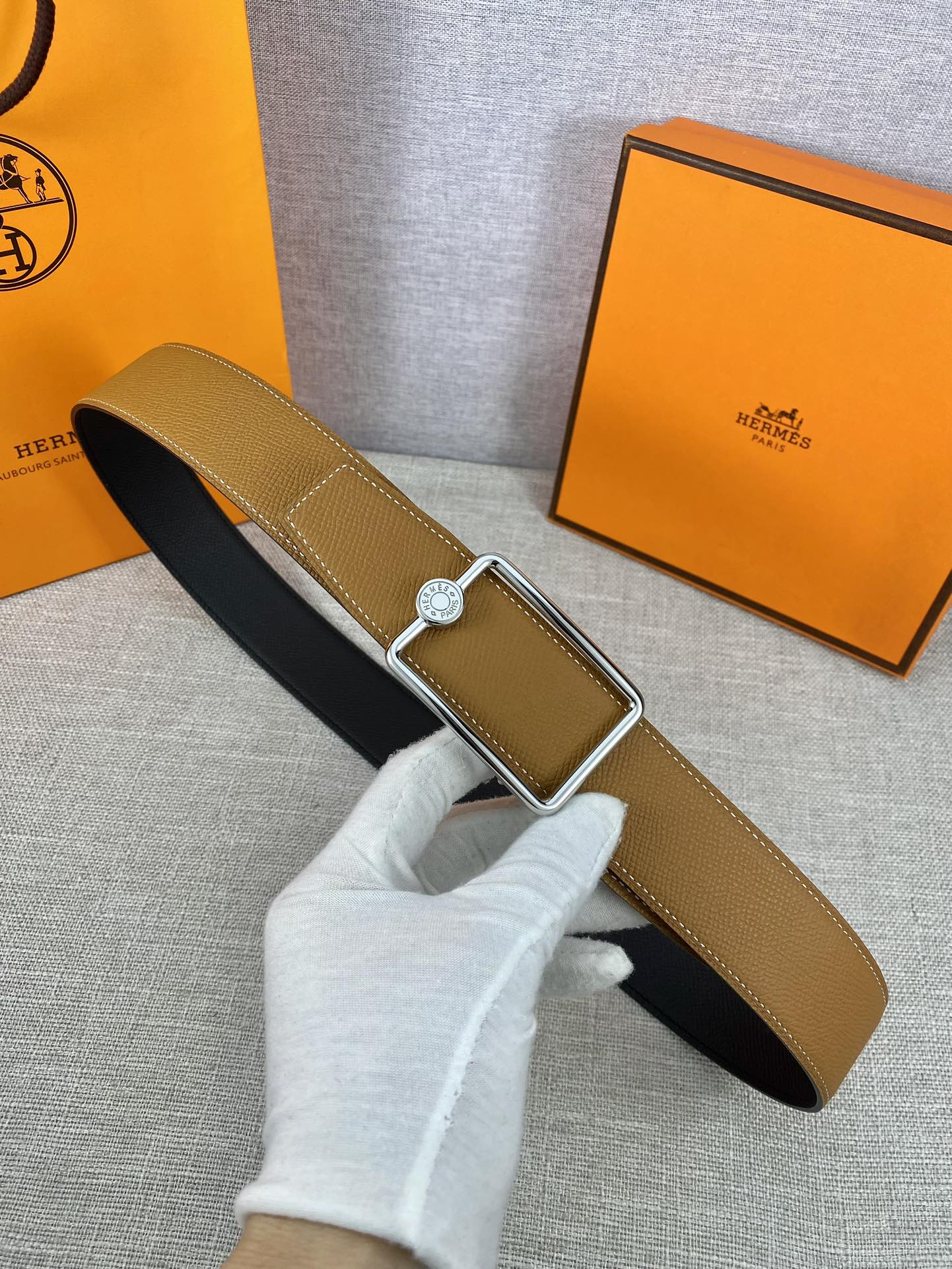 Tan leather belt with gold-tone square buckle and round logo plate