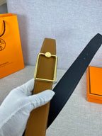 Tan leather belt with gold-tone square buckle and round logo plate, held up