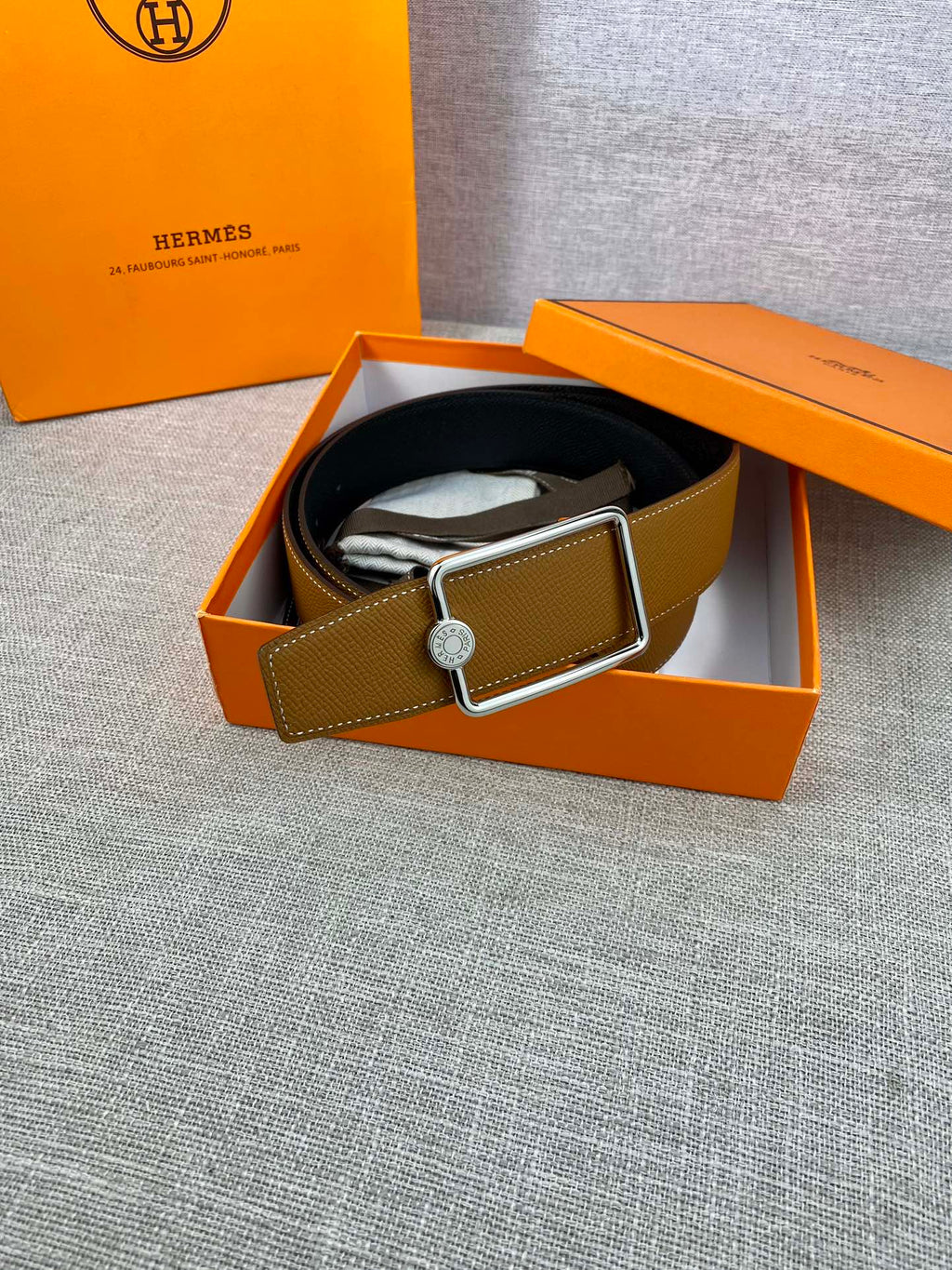 Tan leather belt laid in box with gold-tone square buckle and logo button
