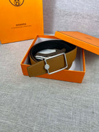 Tan leather belt laid in box with gold-tone square buckle and logo button