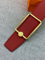 Hermes belt close-up: red leather strap with gold buckle and round emblem charm