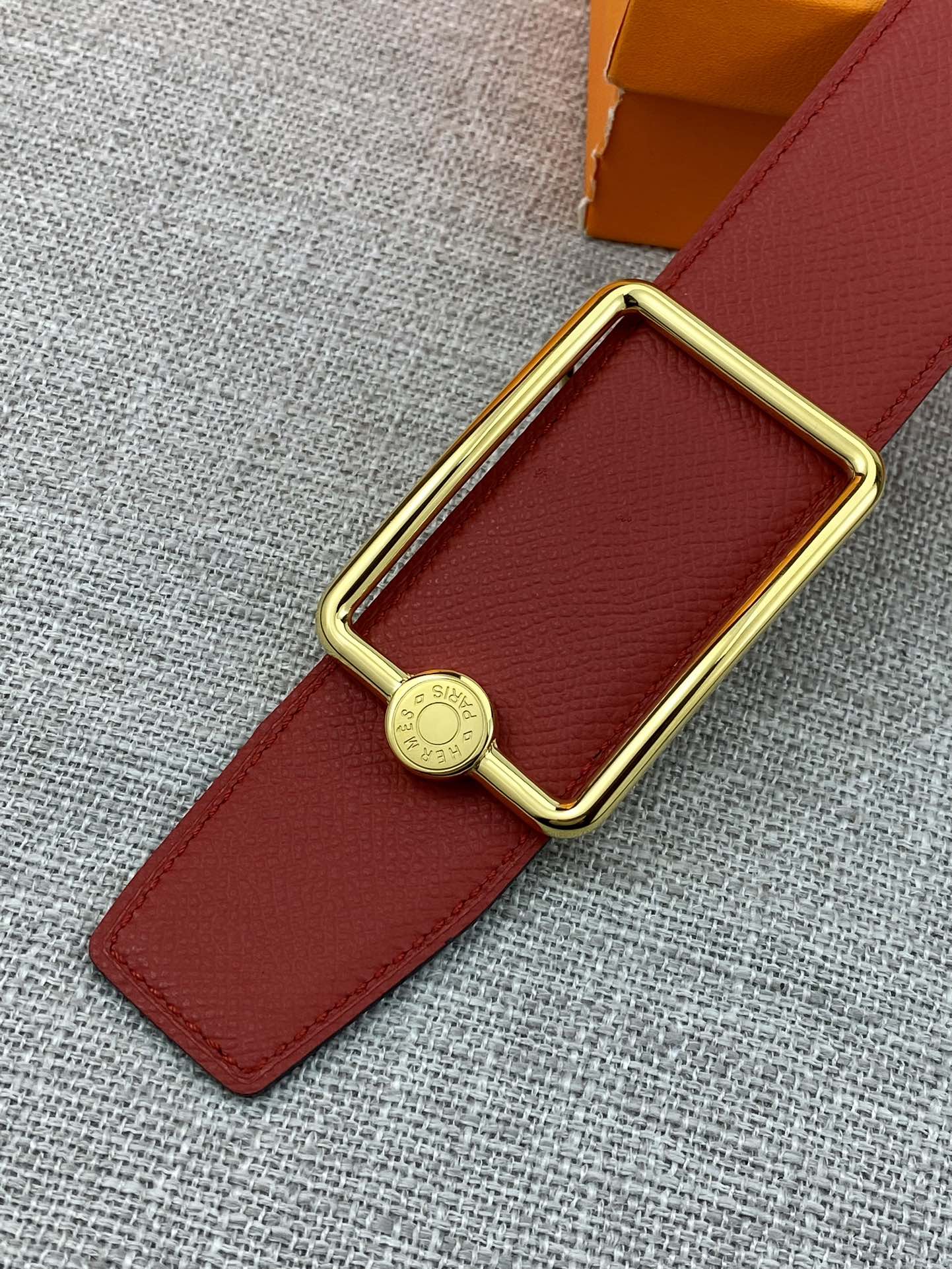 Hermes belt close-up: red leather strap with gold buckle and round emblem charm