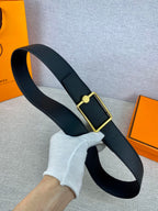 Navy leather belt held in hand with gold rectangular buckle