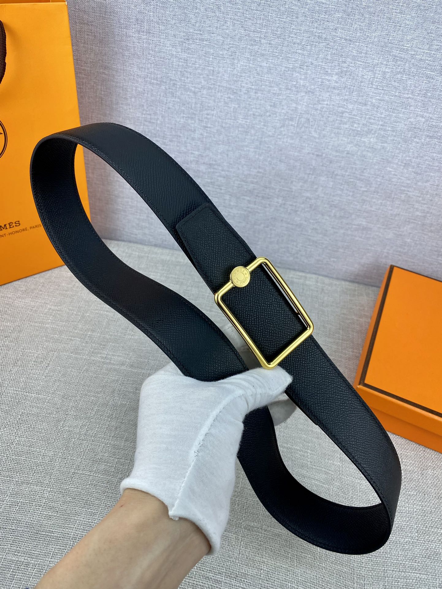 Navy leather belt held in hand with gold rectangular buckle
