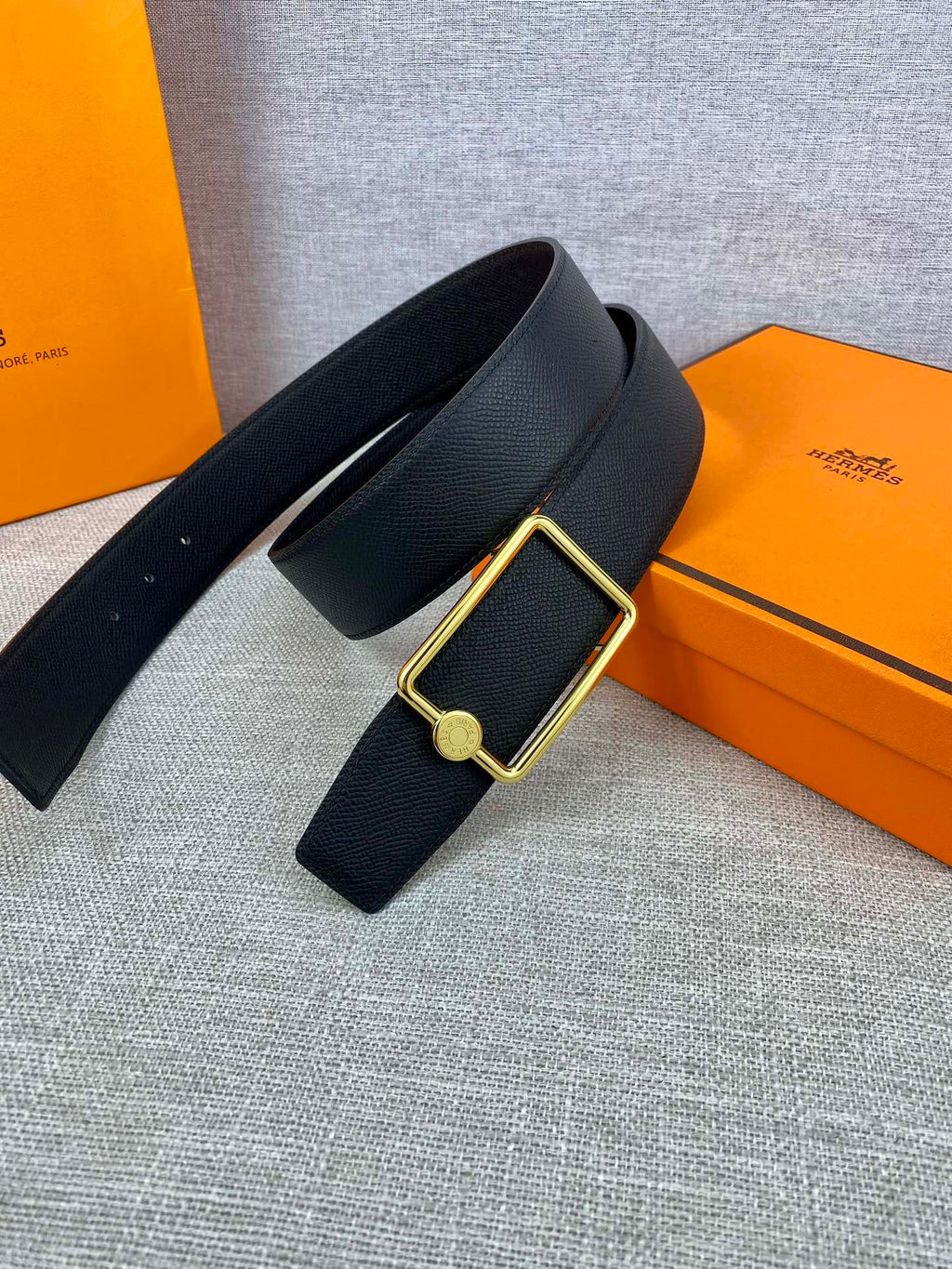 Navy leather belt laid flat with gold rectangular buckle and round emblem