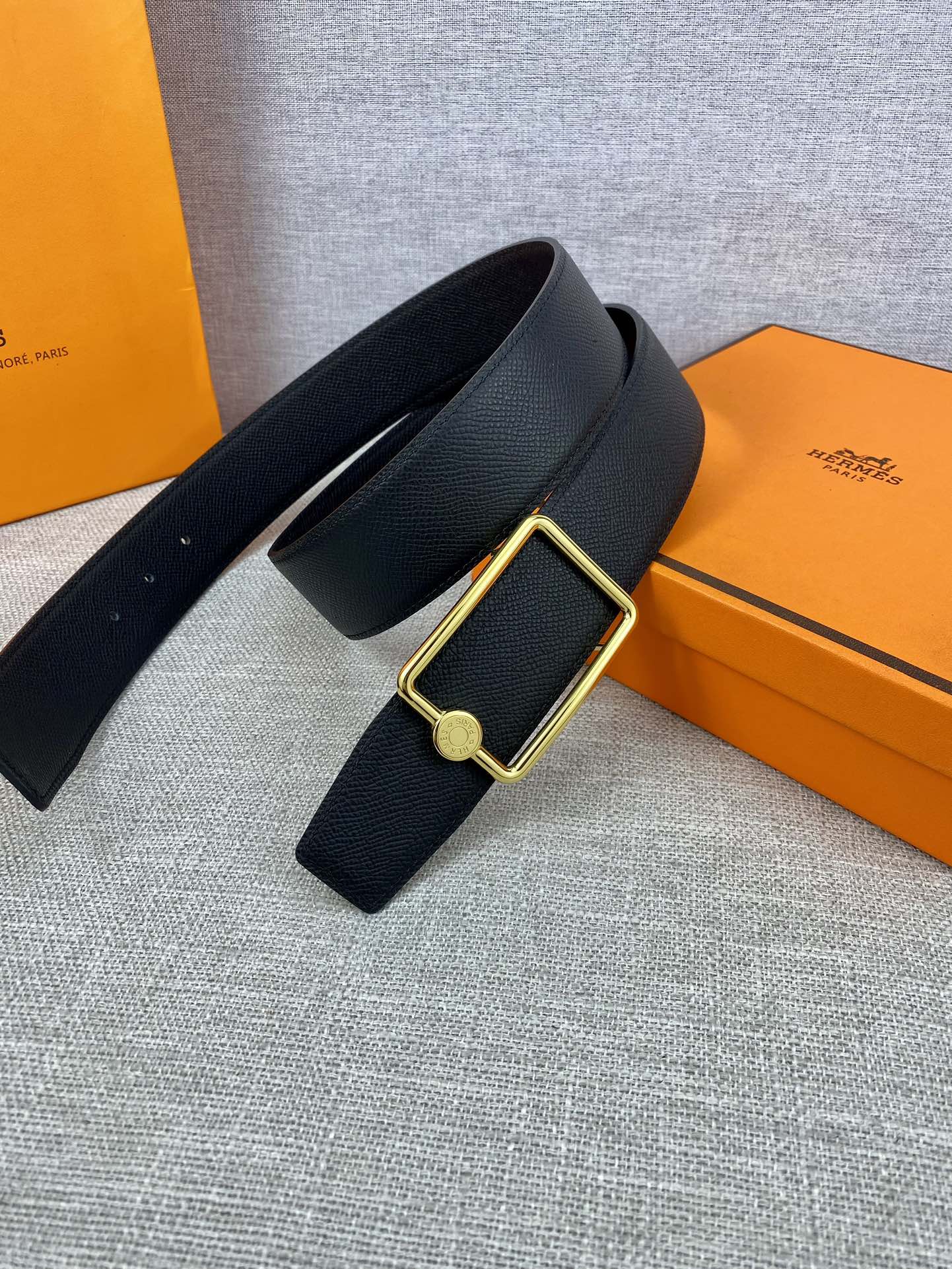 Navy leather belt laid flat with gold rectangular buckle and round emblem