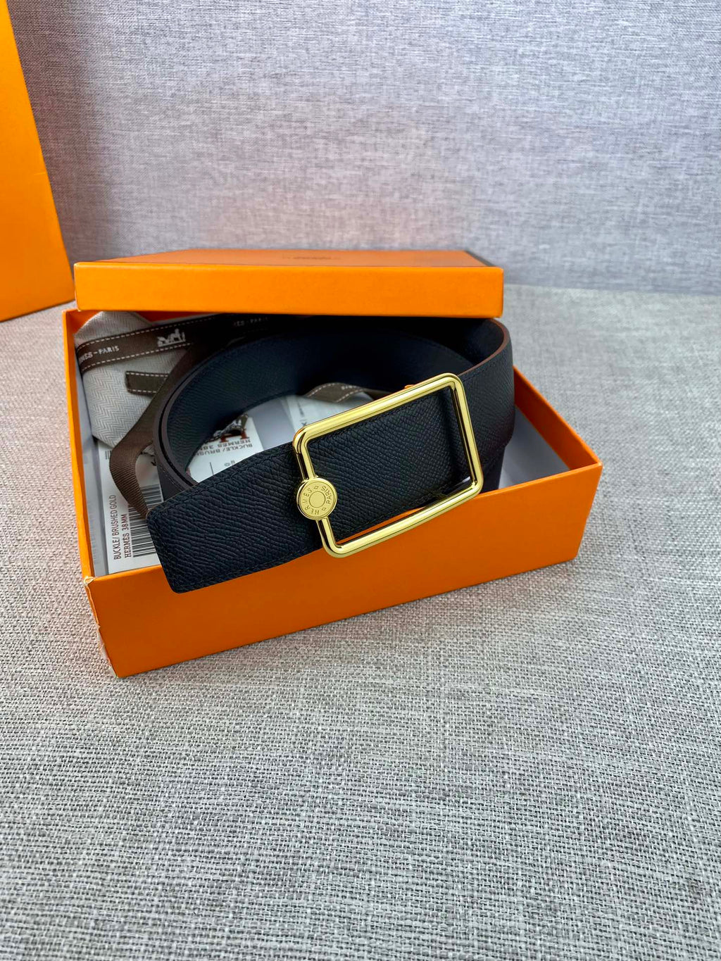 Navy leather belt with gold rectangular buckle and round engraved charm