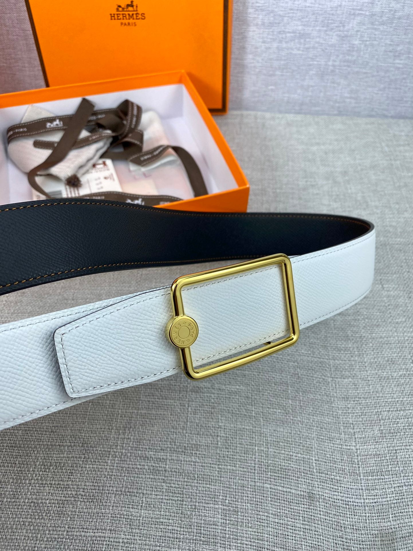 Light blue leather belt detail with gold buckle, round charm, and keeper flap.