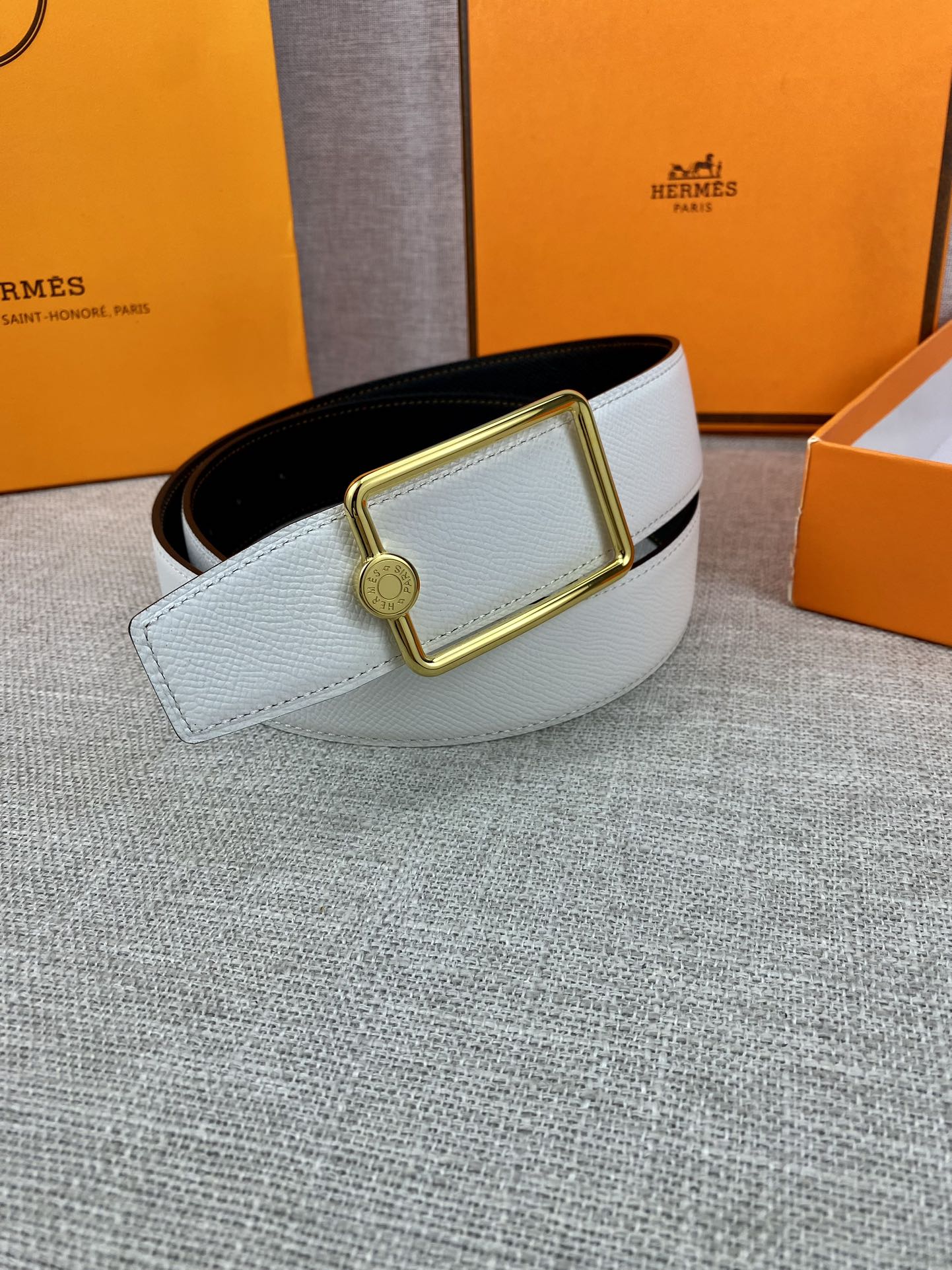 Light blue leather belt with gold rectangular buckle resting on a belt box.