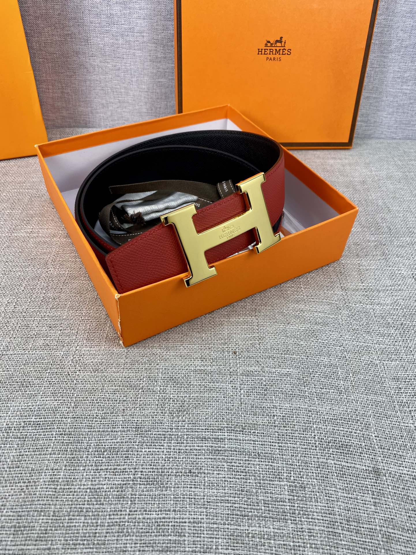 Hermes belt inside a gift box: red leather with gold-tone H buckle and black lining