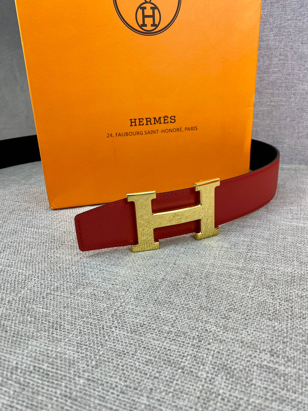 Hermes belt with red strap and gold-tone H buckle against a flat surface