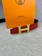 Hermes belt with red strap and gold-tone H buckle against a flat surface