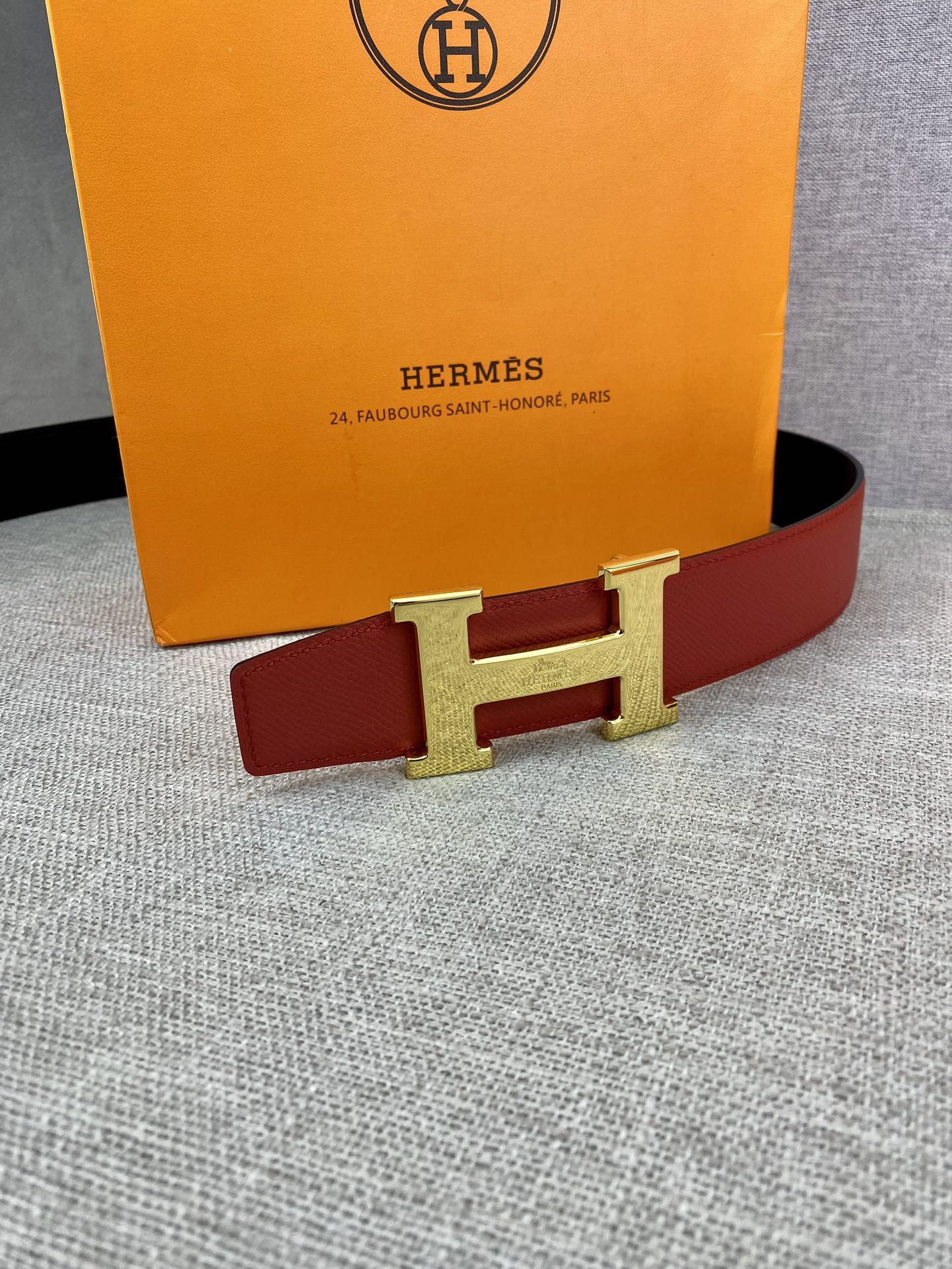 Hermes belt with red strap and gold-tone H buckle against a flat surface