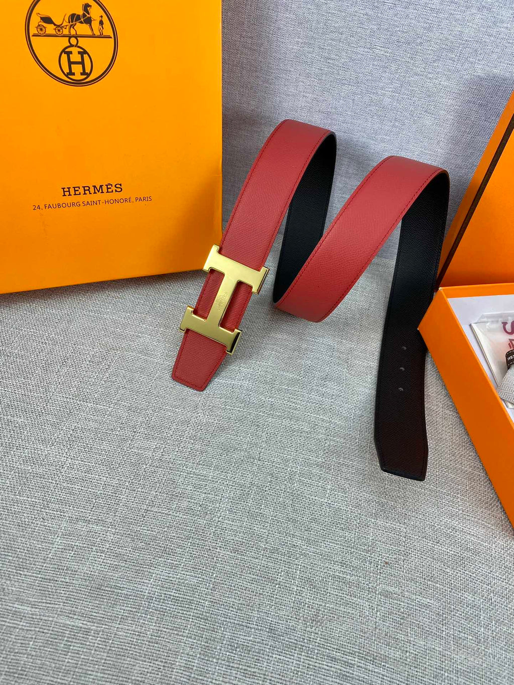 Hermes belt pair view: red leather with gold-tone H buckle, black underside visible