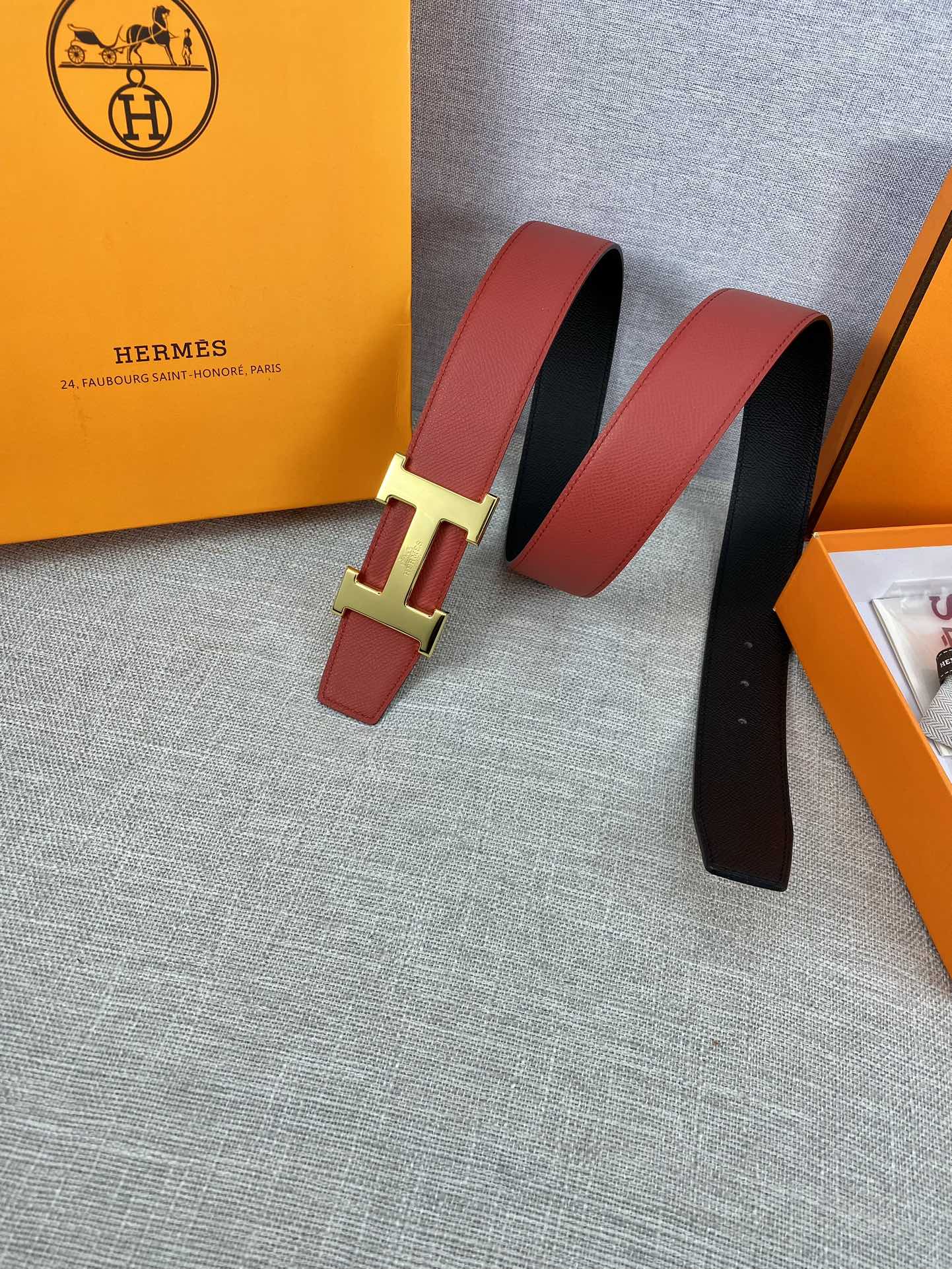 Hermes belt pair view: red leather with gold-tone H buckle, black underside visible