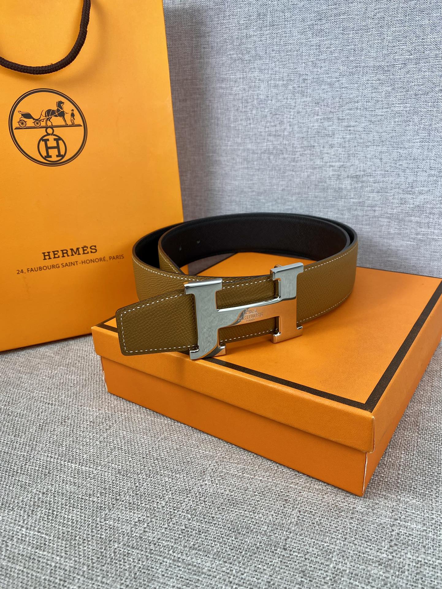 Hermes belt resting on box: tan strap with gold buckle and dark underside