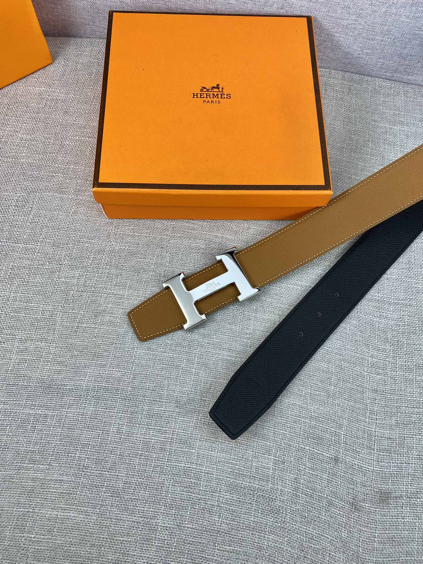 Hermes belt with tan strap and gold buckle, navy strap end on box