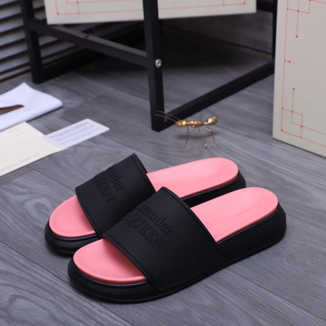 Slide sandals pair with black upper and pink footbeds, strap band shows embossed logo text