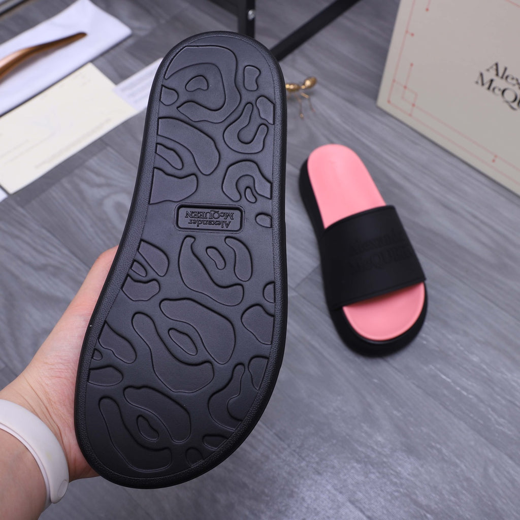 Outsole view of black slide sandal with textured tread; hand holding over pink slide sandal
