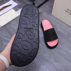 Outsole view of black slide sandal with textured tread; hand holding over pink slide sandal