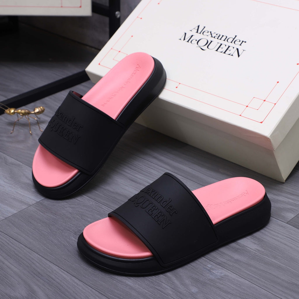 Two slide sandals on floor; black straps, pink footbeds, embossed Alexander McQUEEN on bands