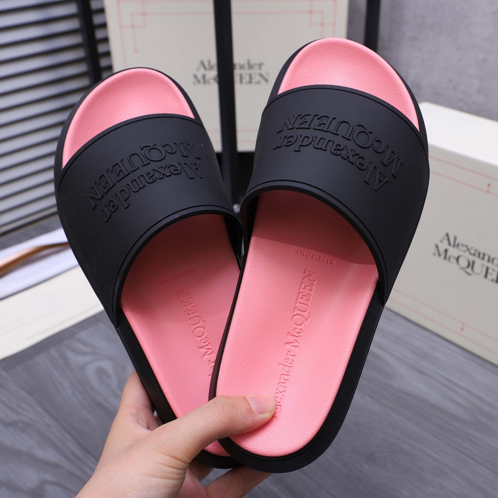 Close-up of slide sandals with black straps over pink footbeds; embossed logo text on straps