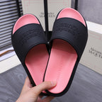 Close-up of slide sandals with black straps over pink footbeds; embossed logo text on straps