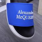 Alexander McQueen slide sandal close-up, blue logo strap over black upper with white trim