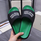 Green slide sandals held in hand with black strap and Alexander McQueen text