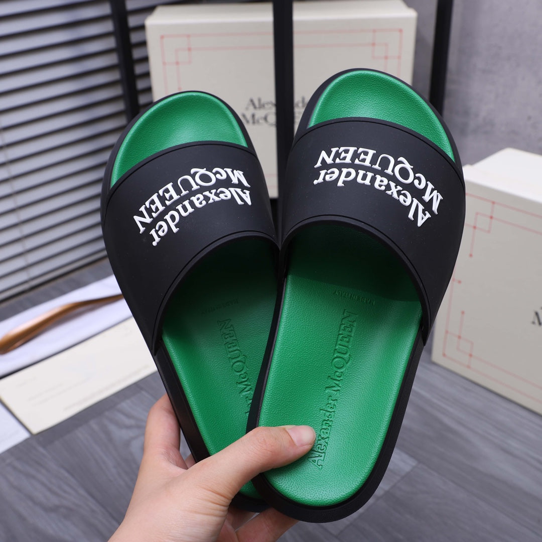 Green slide sandals held in hand with black strap and Alexander McQueen text