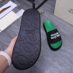 Black slide sandal outsole with textured pattern; green slide sandals behind