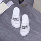 Alexander McQueen white leather slide sandals with logo straps facing camera, pair