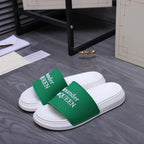 White slide sandals with green logo straps, side view
