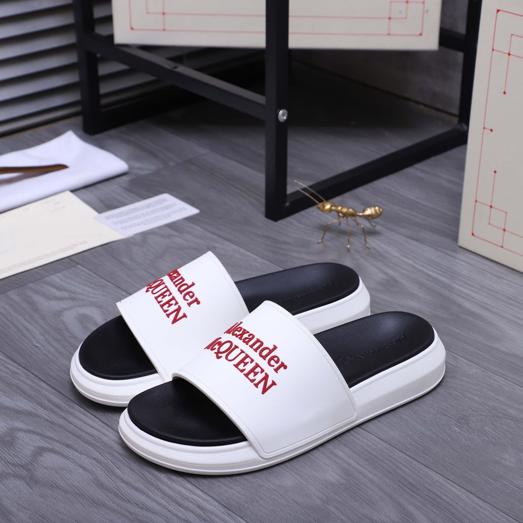 Black-and-white slide sandals with wide white strap and Alexander McQueen logo.